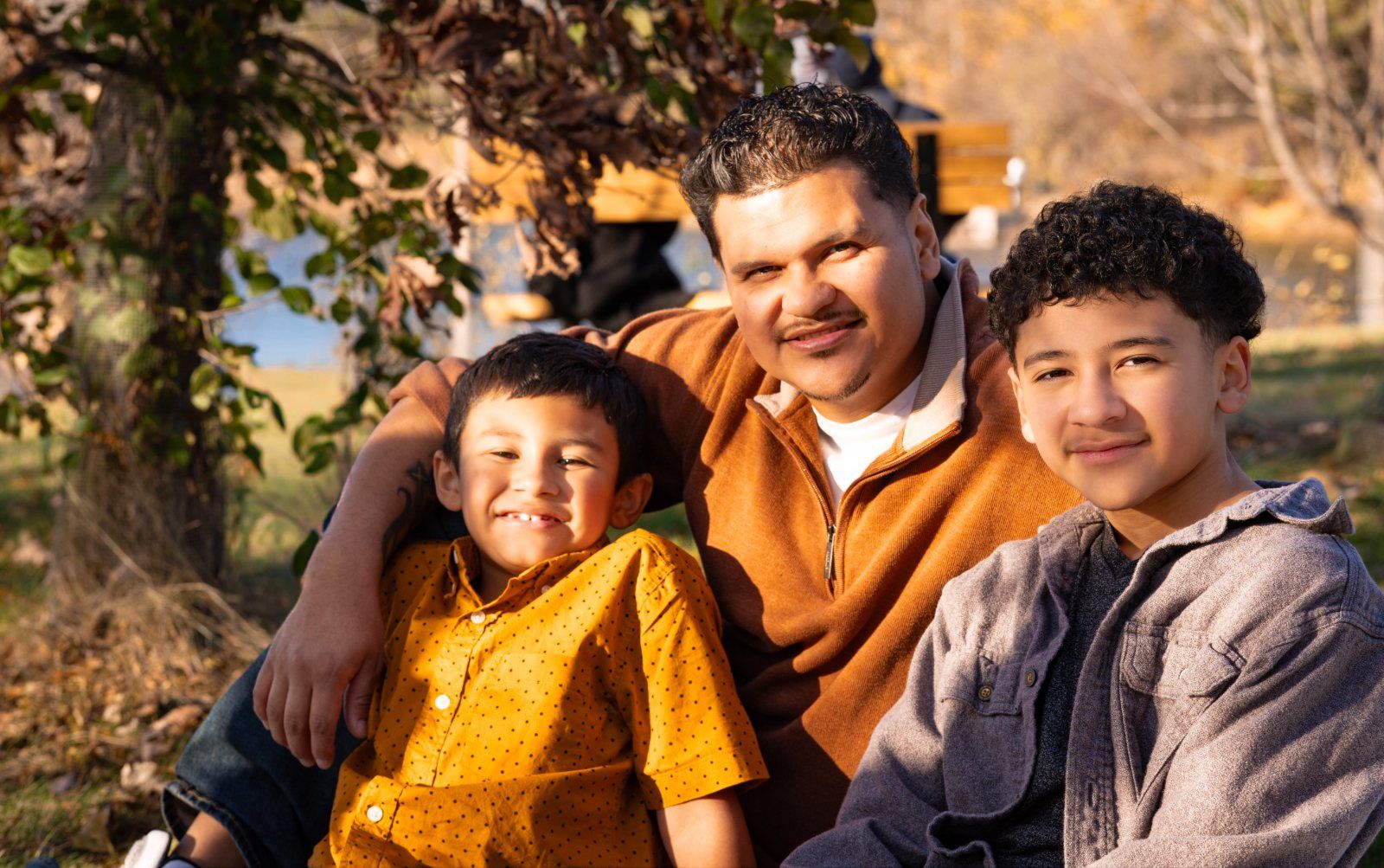A father and his two sons smiling together by the lake at golden hour
