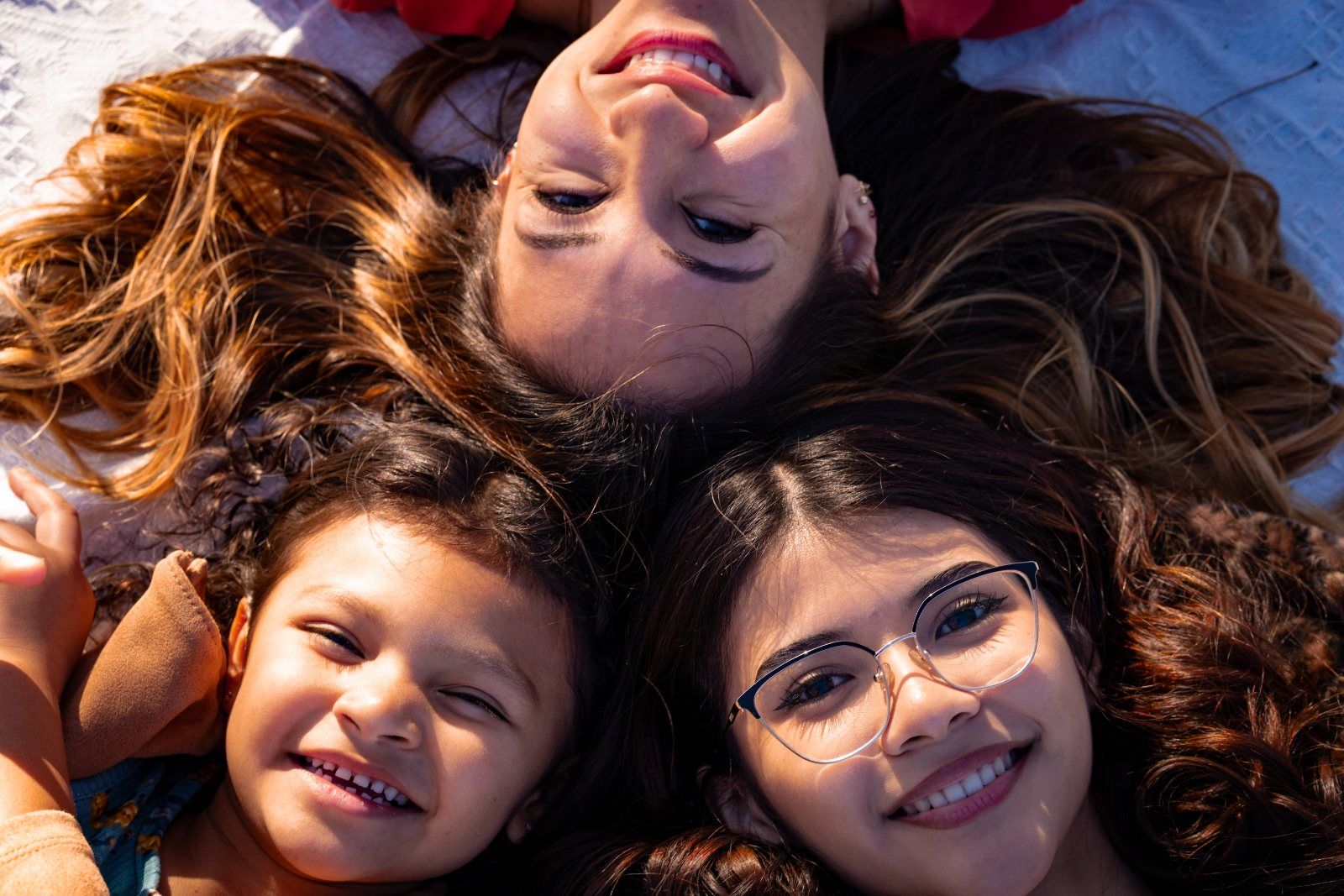 A mother and her two daughters lying head to head in the grass, smiling up at the camera