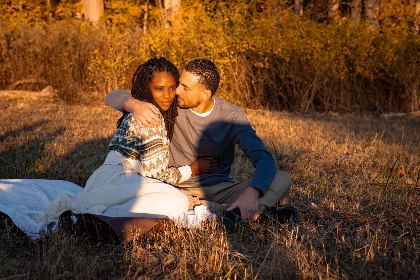 A couple sitting close on a blanket in golden autumn grass